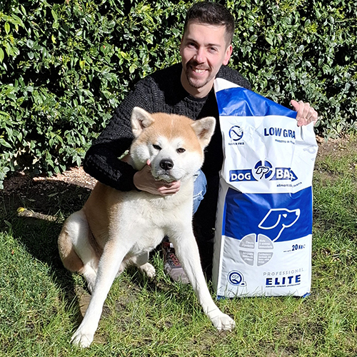 Uomo accovacciato con due cani Boxer e sullo sfondo sacco di crocchette Dogbauer